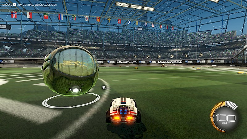 Ein Screenshot von Rocket League. Es wird ein Auto in der Arena gezeigt, links davor befindet sich ein doppelt so großer Spielball. Er hat eine Metall-Optik und reflektiert deshalb die grüne Farbe des Spielfelds. Zwischen Auto und Ball befindet sich ein k