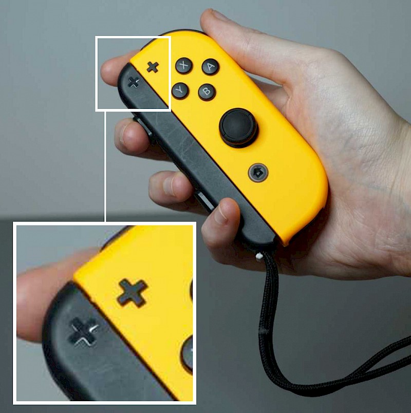 Ein Joy-Con mit eingesteckter Schlaufe. Auf beiden ist ein Plus Symbol.