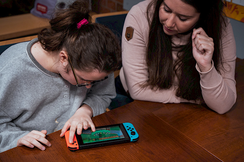 Eine Spieletesterin spielt an der Nintendo Switch. Eine Medienpädagogin sitzt daneben.