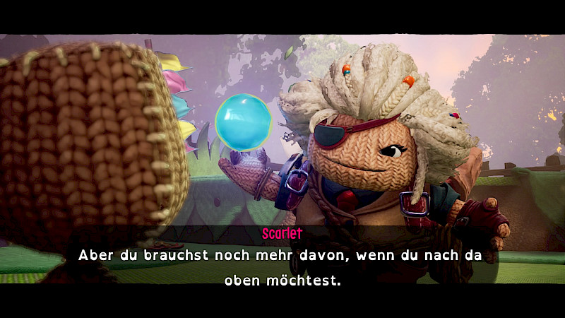 Eine Strickfigur mit weißen Haaren und Augenklappe hält eine Träumerkugel in der Hand. In den Untertiteln steht: Scarlet: Aber du brauchst noch mehr davon, wenn du nach da oben möchtest.