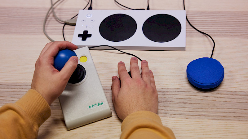 Ein Jugendlicher steuert mit dem Adaptive Controller. Er nutzt Buttons und einen Analogstick von Optima.