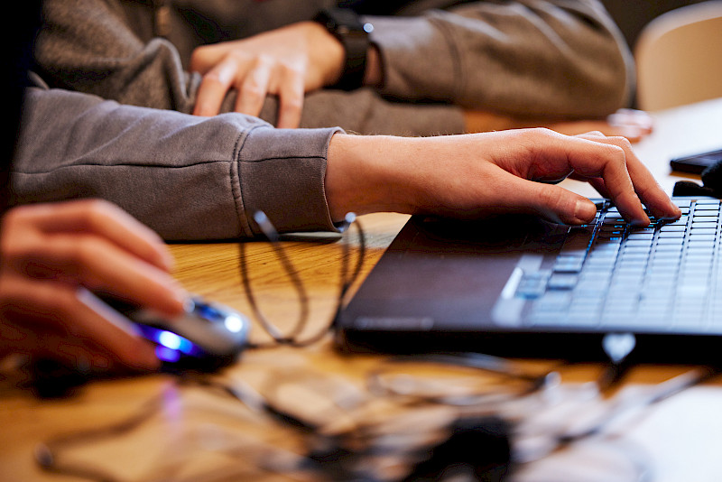 Hände von Jugendlichen schreiben etwas auf einer Laptop-Tastatur.