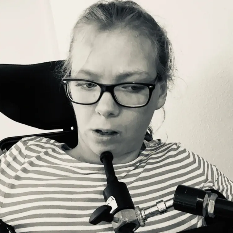 Marlene mit einem Kinn-Joystick. Sie hat helle Haare und trägt eine Brille. Das Bild ist schwarz-weiß.