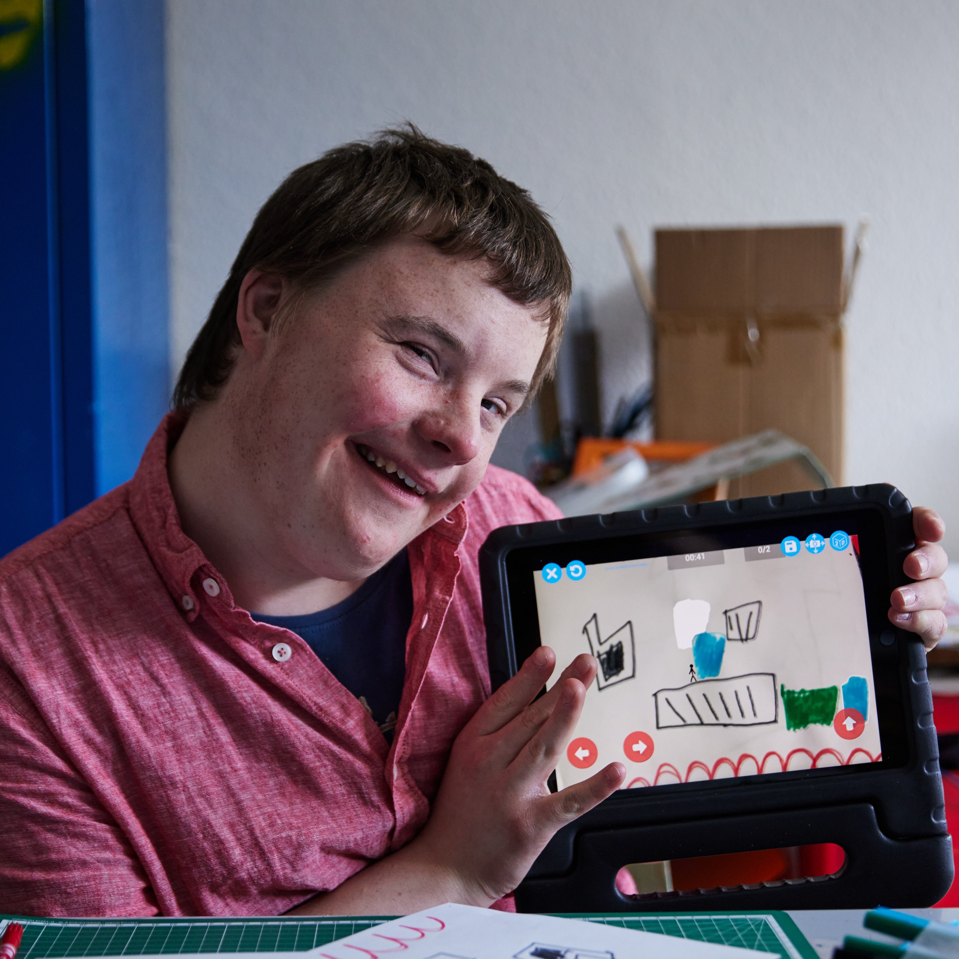 Ein Junge hält ein Tablet in der Hand. Darauf ist ein gemaltes Spiel zu sehen.