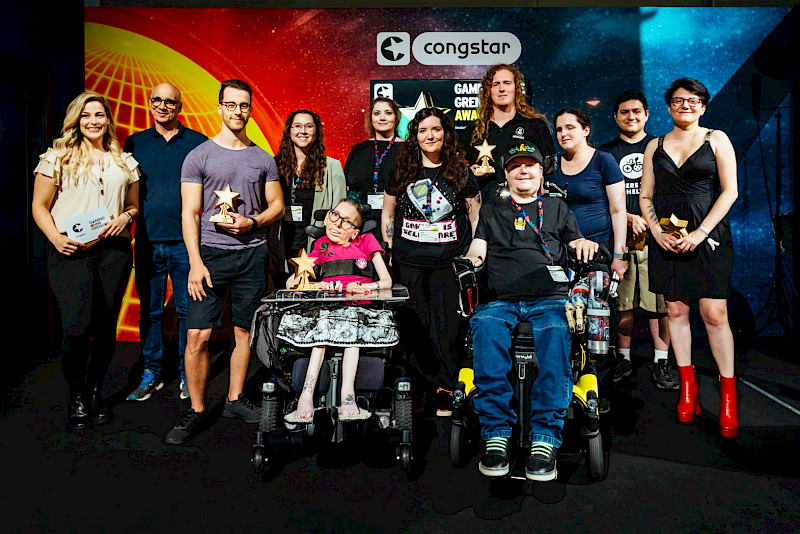 Viele verschiedene Personen stehen auf einer Bühne. Einige halten einen Pokal in der Hand. Es sind alle Beteiligten des Gaming ohne Grenzen Awards.