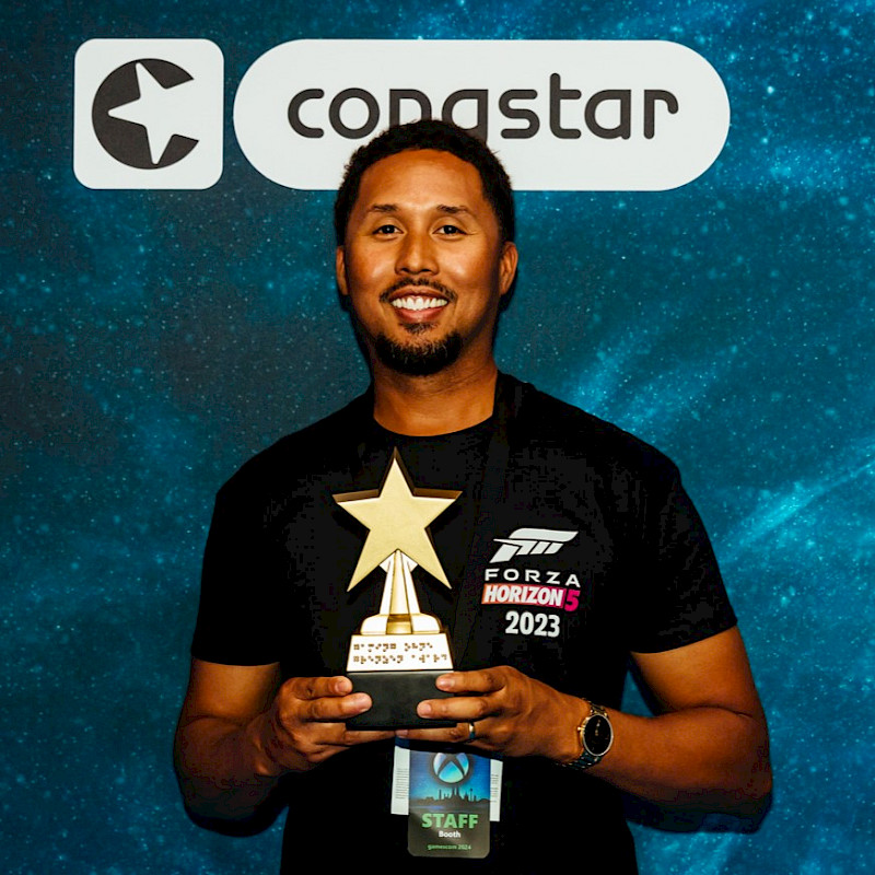 Eine männliche Person von Forza Motorsport hält den goldenen, sternförmigen Pokal in der Hand.