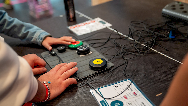 Es liegen Buttons auf einem Tisch. Sie werden von zwei Personen mit den Händen gedrückt.
