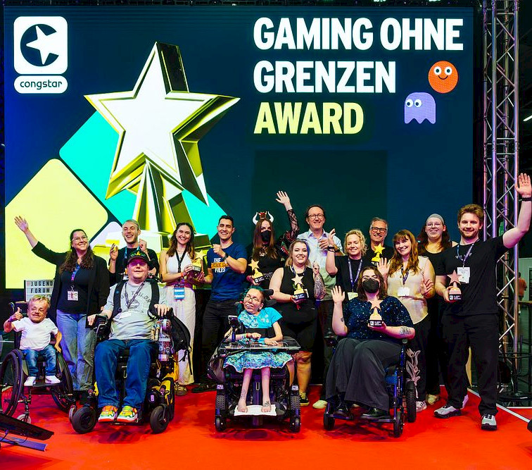 Ein Foto von allen Laudator*innen und Gewinner*innen des Gaming ohne Grenzen Awards 2025. Sie freuen sich und winken in die Kamera.