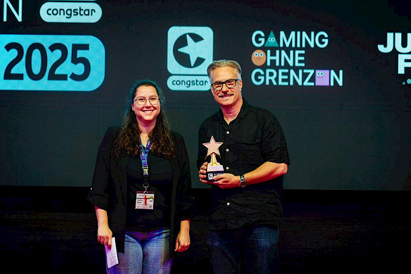 Auf dem Foto sind Saskia Moes von Gaming ohne Grenzen und John Tyrell vom Devolver Digital Marketing Team. John hat den Community Choice Award für das Spiel Der Kühne Knappe bekommen.