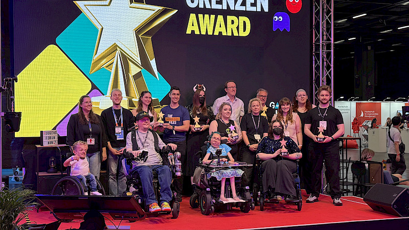 Auf dem Bild sind mehrere Personen. Sie haben einen Gaming ohne Grenzen Award gewonnen. Die Personen stehen auf einer Bühne auf der Gamescom.