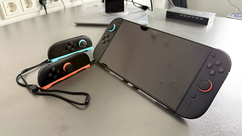Die Switch 2 steht auf einem grauen Tisch. Neben ihr liegen zwei Joycon.
