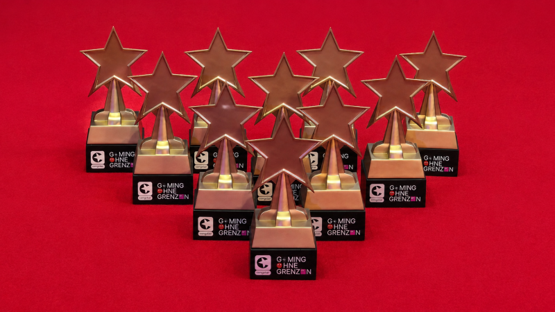 Neun goldene Stern-Trophäen des „Gaming ohne Grenzen Award“ stehen auf rotem Untergrund, teilweise hintereinander angeordnet.